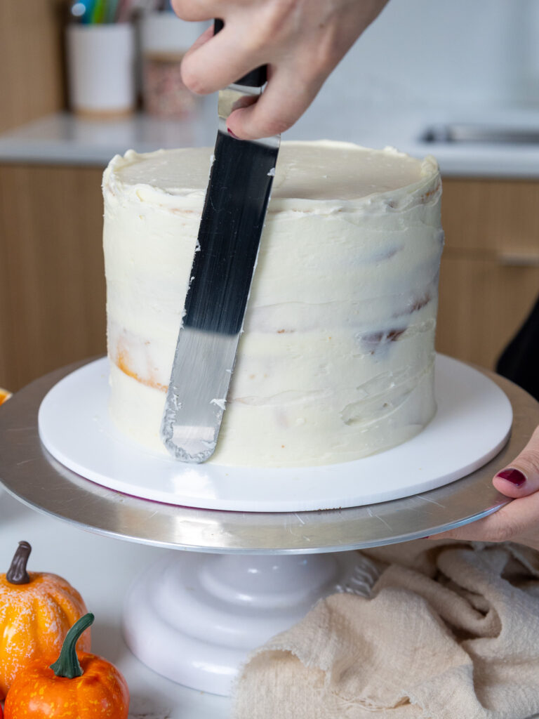 image of a pumpkin caramel cake being crumb coated with a large offset spatula
