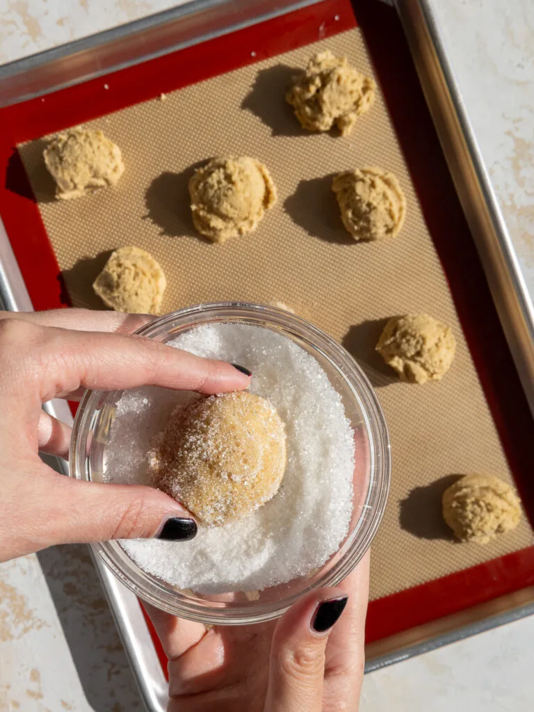 image of brown butter sugar cookies being coated in sanding sugar before being baked