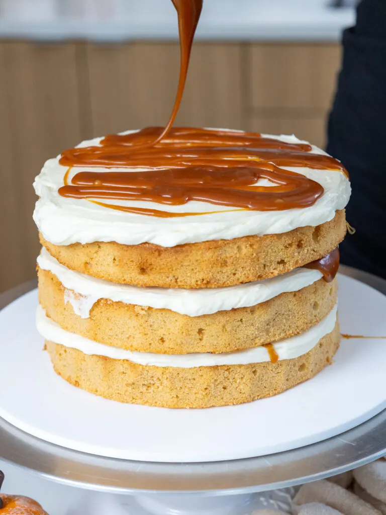 image of caramel being drizzled between the layers of a pumpkin caramel cake