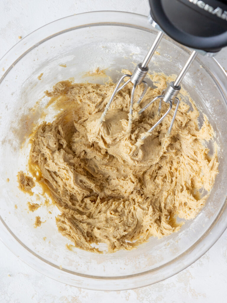image of brown butter sugar cookie dough that's been mixed in a glass bowl with an electric mixer
