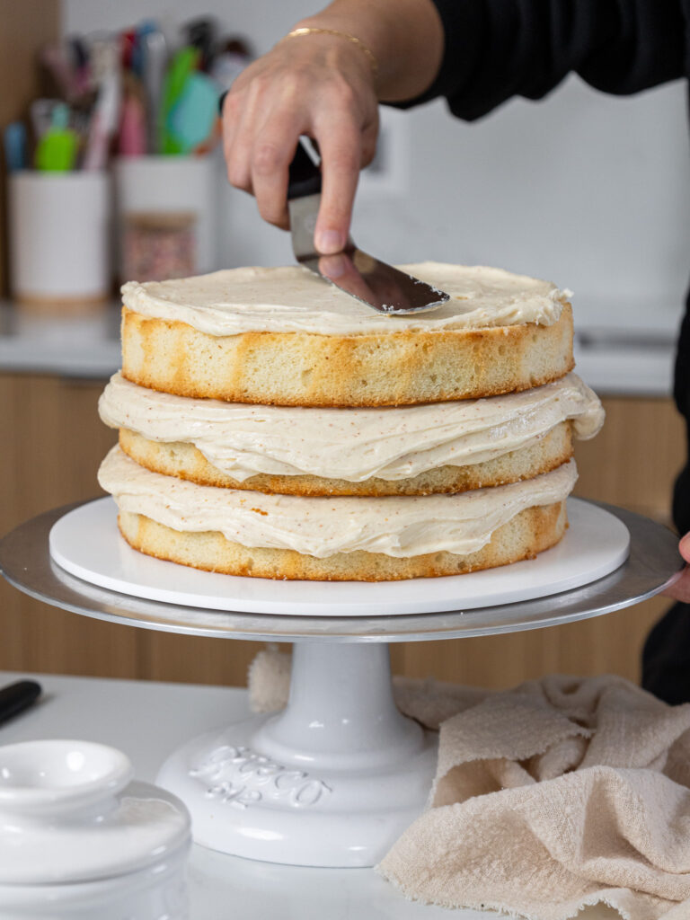 image of a brown butter cake being frosted and stacked on a cake stand