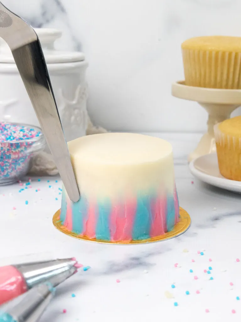 image of pink and blue frosting being spread on a mini cake with a small offset spatula
