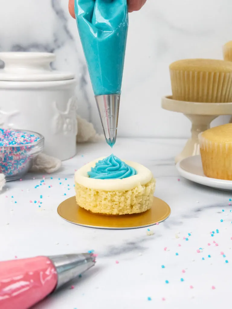 image of a cupcake that's been cut in half and is being filled with blue frosting