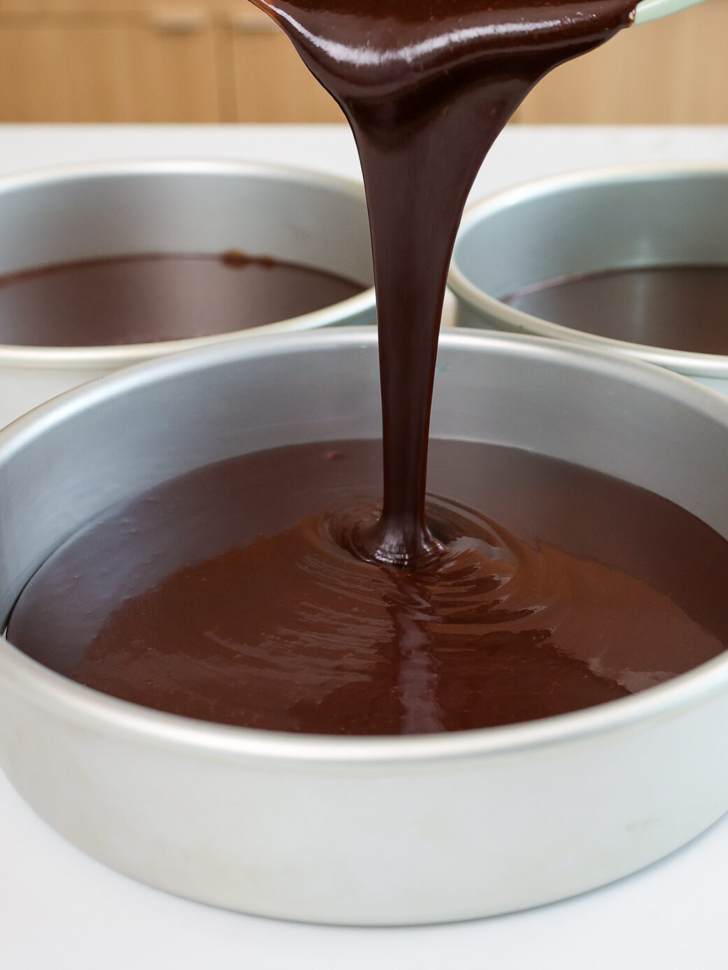 image of dark chocolate cake batter being poured into cake pans