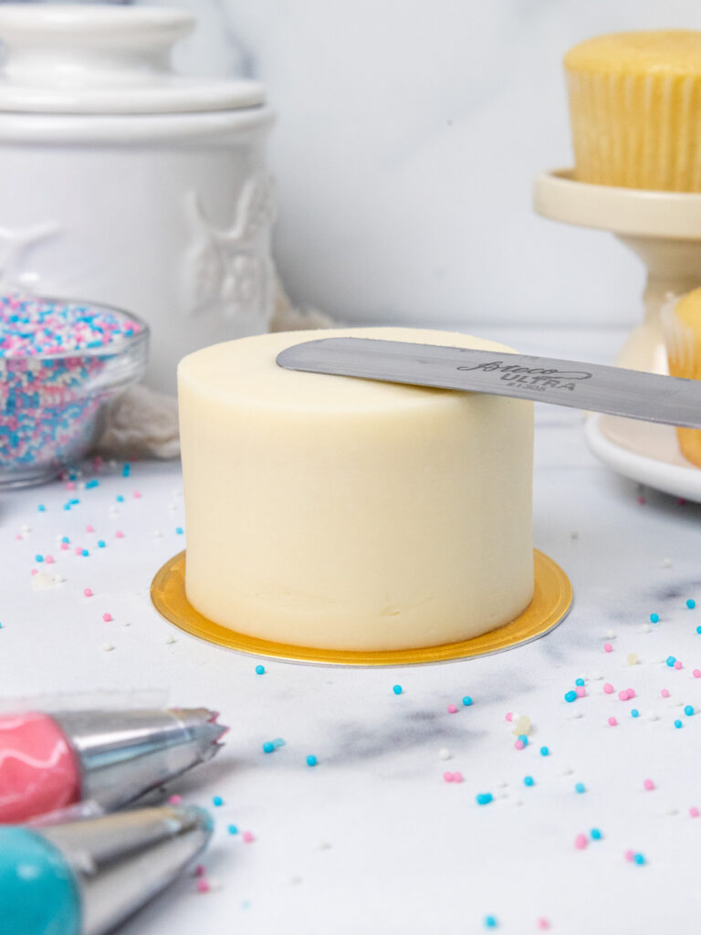 image of frosting being smoothed onto a cupcake that's been decorated to look like a mini cake
