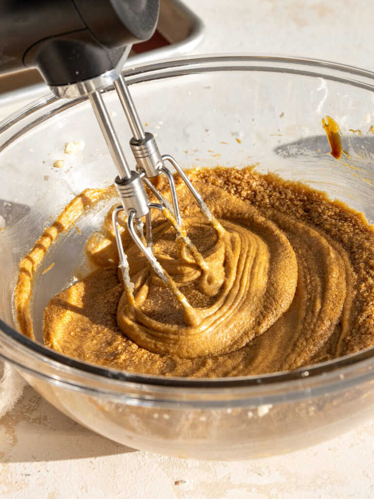 image of molasses and an egg being mixed into gingerbread cookie dough with a hand mixer