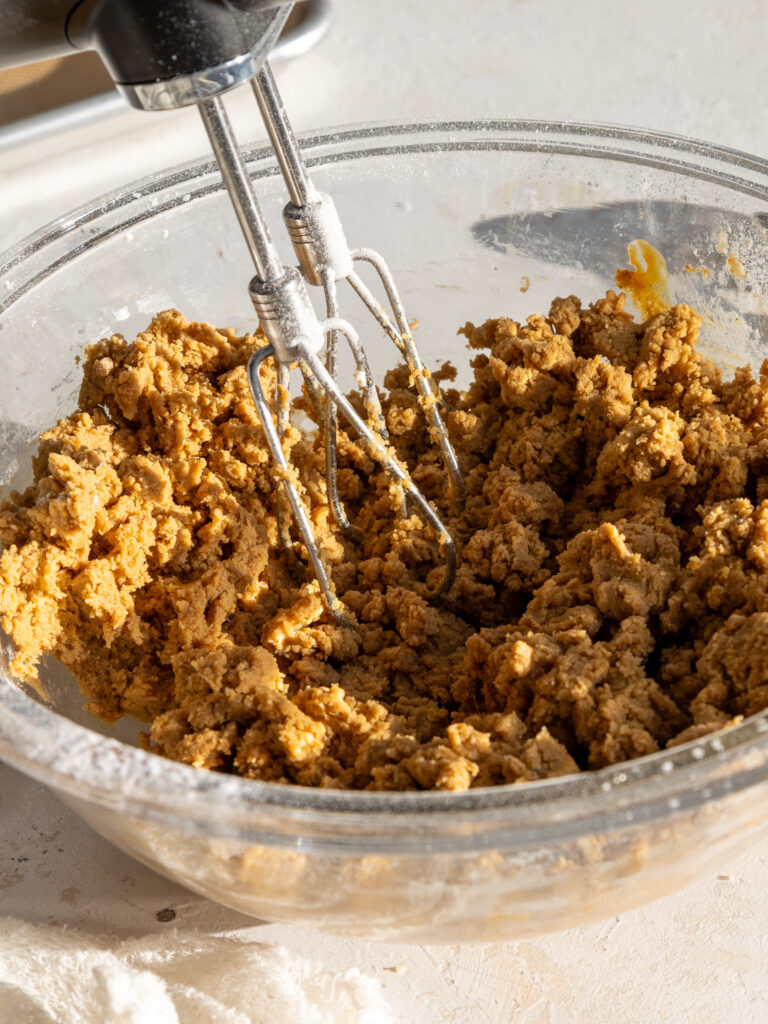 image of gingerbread cookie dough being mixed together with a hand mixer in a glass bowl