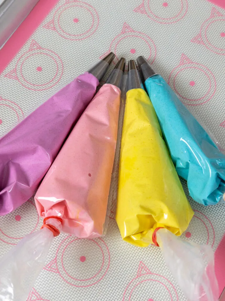 image of purple, pink, yellow, and blue macaron batter in small piping bags