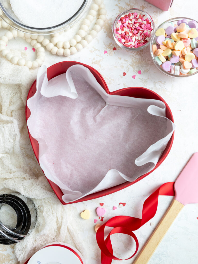 image of a heart shaped box that's been lined with parchment paper before being filled with valentine's day themed desserts