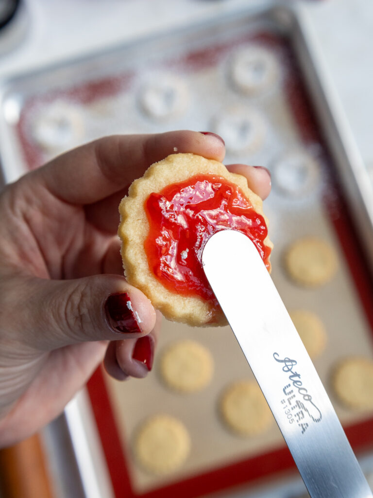 image of raspberry freezer jam being spread onto a raspberry Linzer cookie