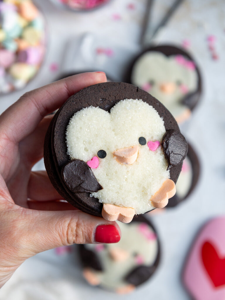 image of a cute penguin cookie being held up that's been decorated with buttercream frosting and sprinkles