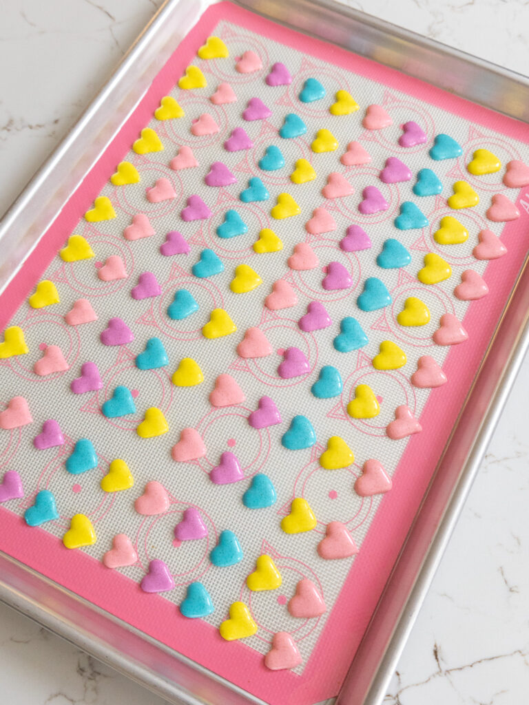 image of mini heart shaped macarons piped on a silicone baking sheet to make cute conversation heart macarons