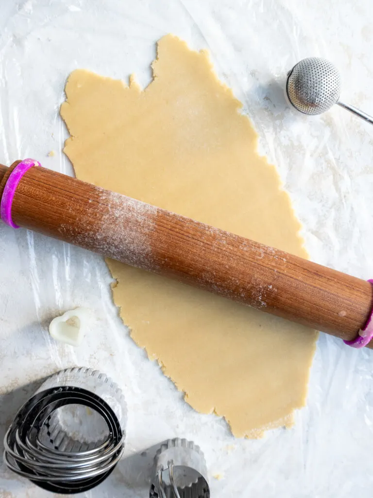 image of Linzer shortbread cookie dough being rolled out with a rolling pin on top of plastic wrap