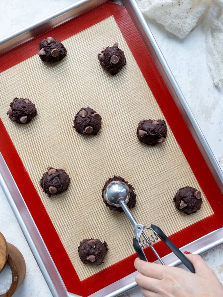 image of double chocolate cookies being scooped onto a silicone lined baking sheet