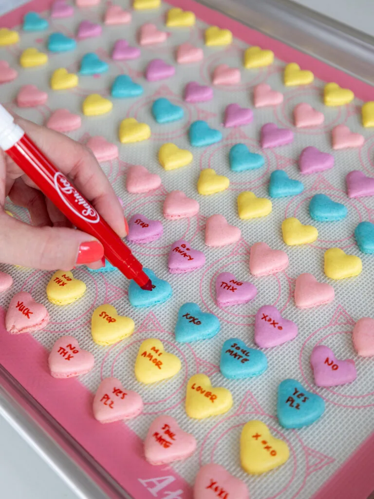 image of conversation heart macaron shells being written on with a red edible marker