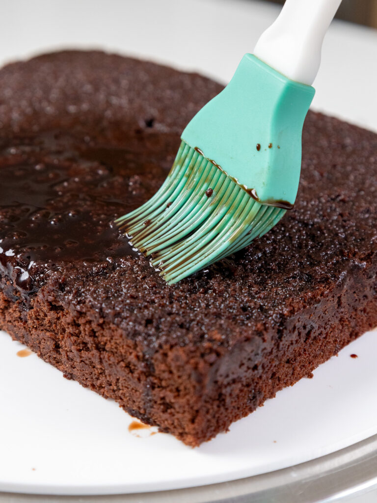 image of a chocolate cake layer being brushed with chocolate simple syrup using a silicone kitchen brush