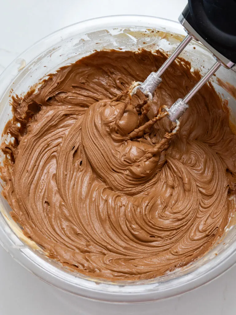 image of chocolate buttercream being mixed in a glass bowl with a hand mixer