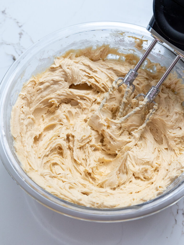 image of peanut butter buttercream being mixed in a glass bowl with an electric hand mixer