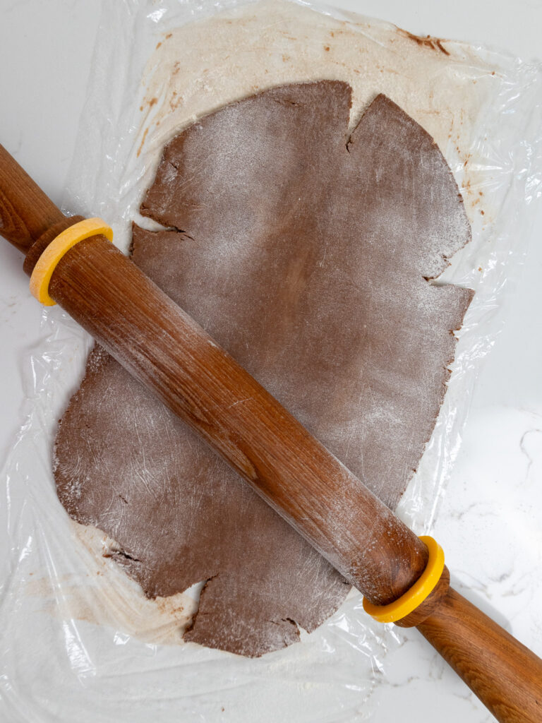 image of chocolate cream cheese cookie dough being rolled out with rolling pin