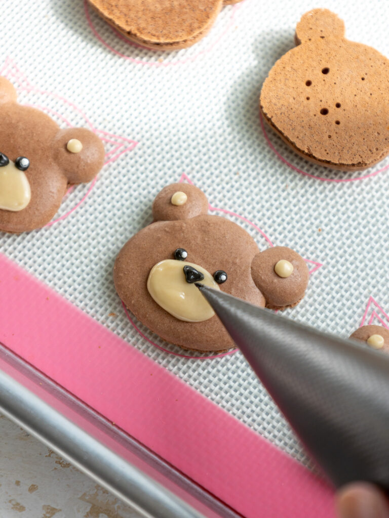 image of black royal icing being piped onto a bear macaron shell