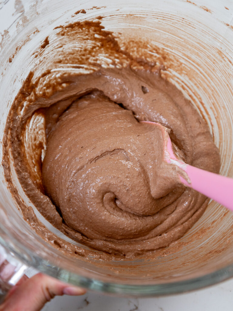 image of dark chocolate macaron batter being folded together with a rubber spatula