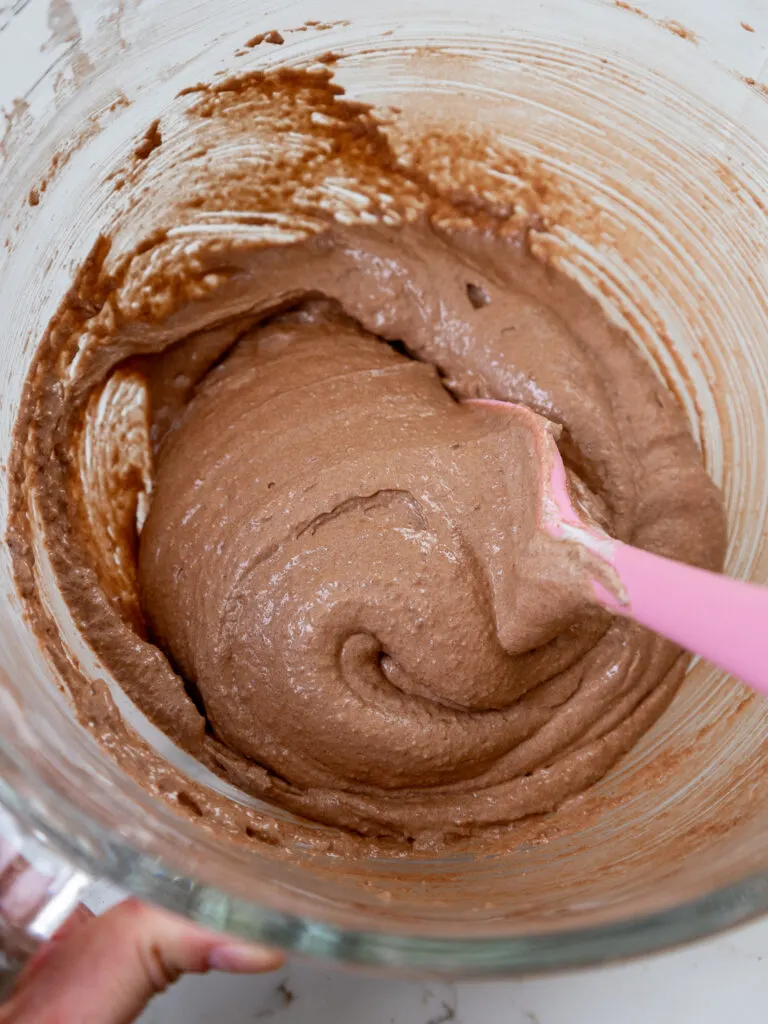 image of dark chocolate macaron batter being folded together with a rubber spatula