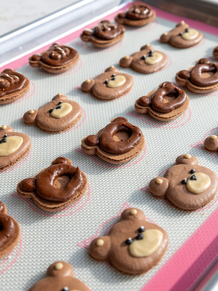 image of teddy bear macarons that have been piped with a ring of dark chocolate ganache