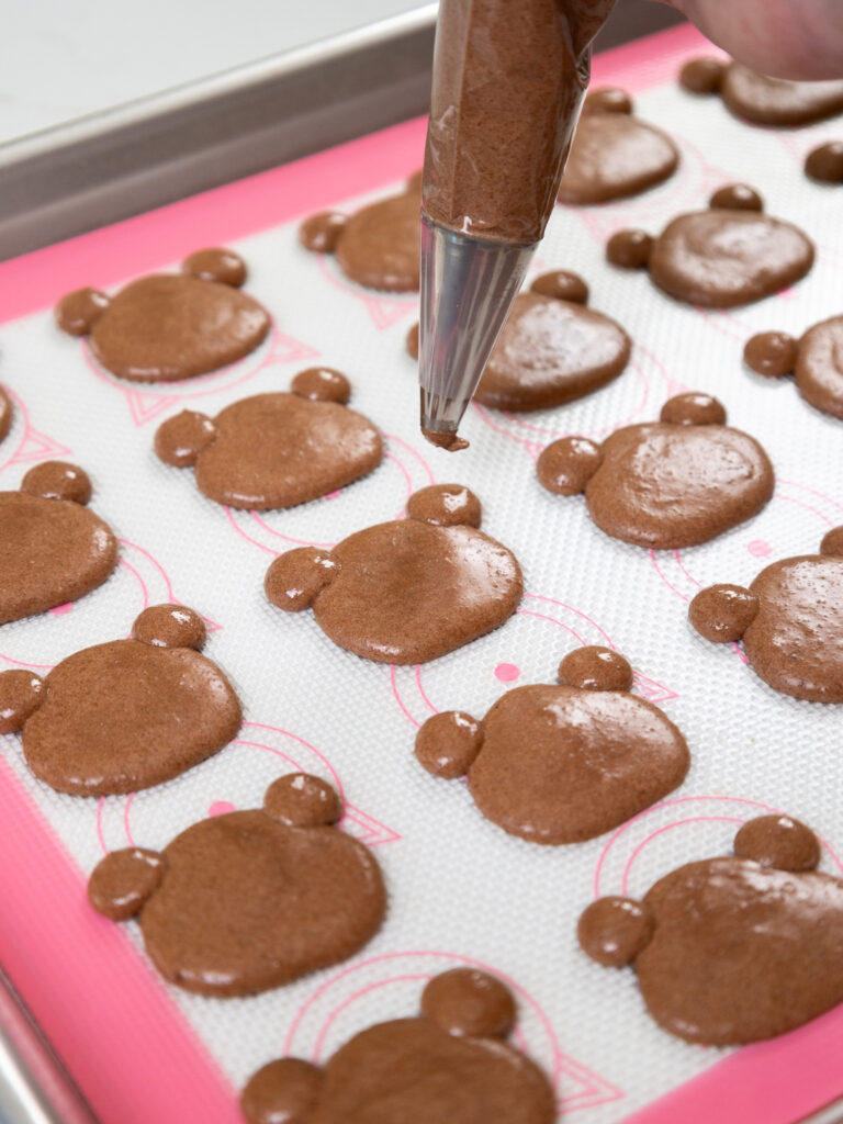 image of bear shaped macaron shells being piped onto a silicone mat