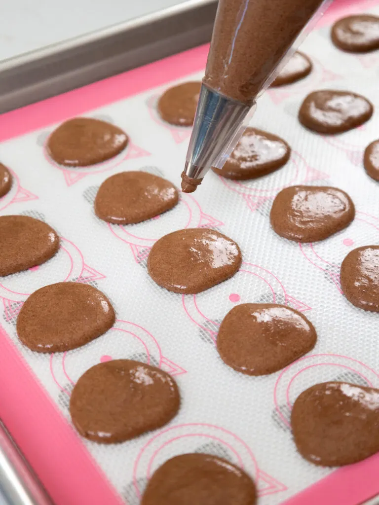 image of bear shaped macaron shells being piped onto a silicone mat