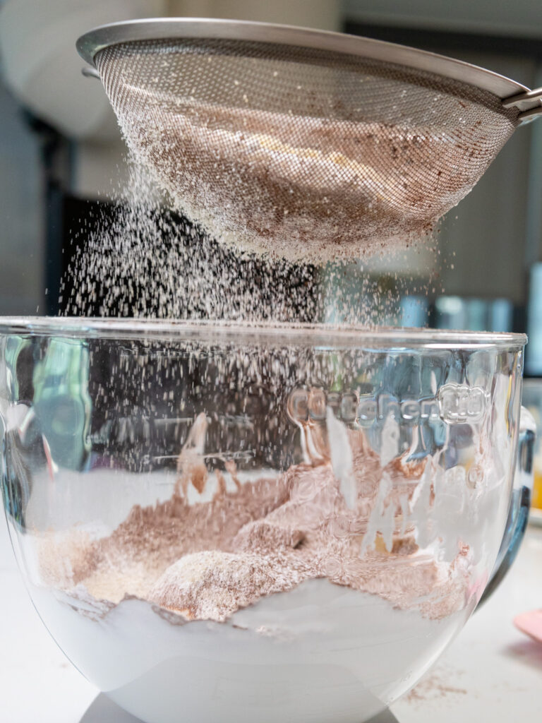 image of dry ingredients being sifted into french meringue to make dark chocolate French macarons