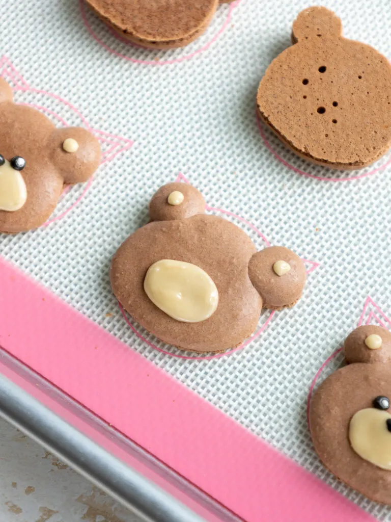image of royal icing being piped onto a macaron shell to make cute teddy bear macarons