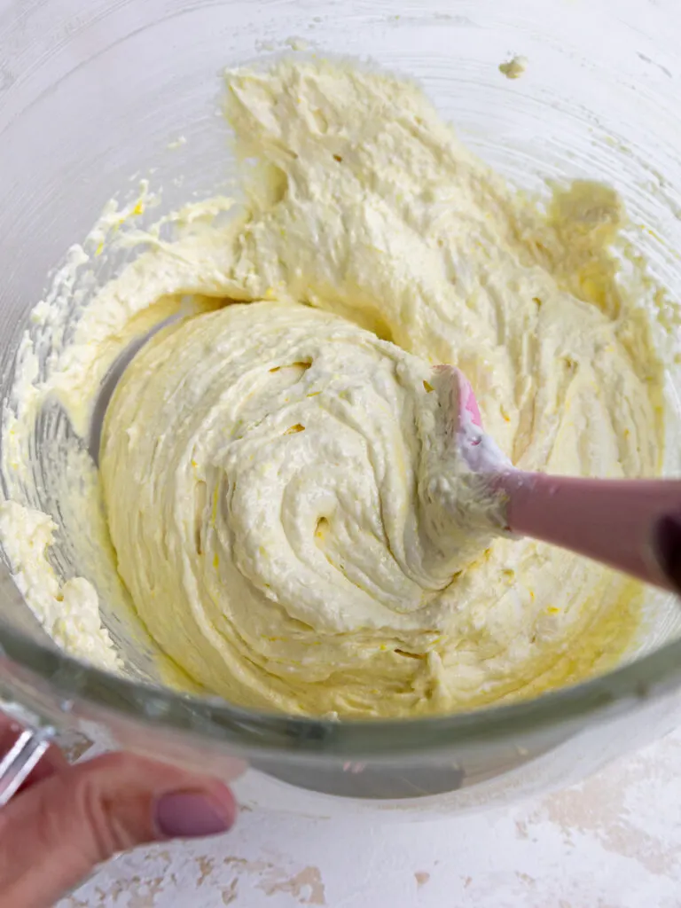 image of light yellow macaron batter being folded together with a rubber spatula in glass bowl
