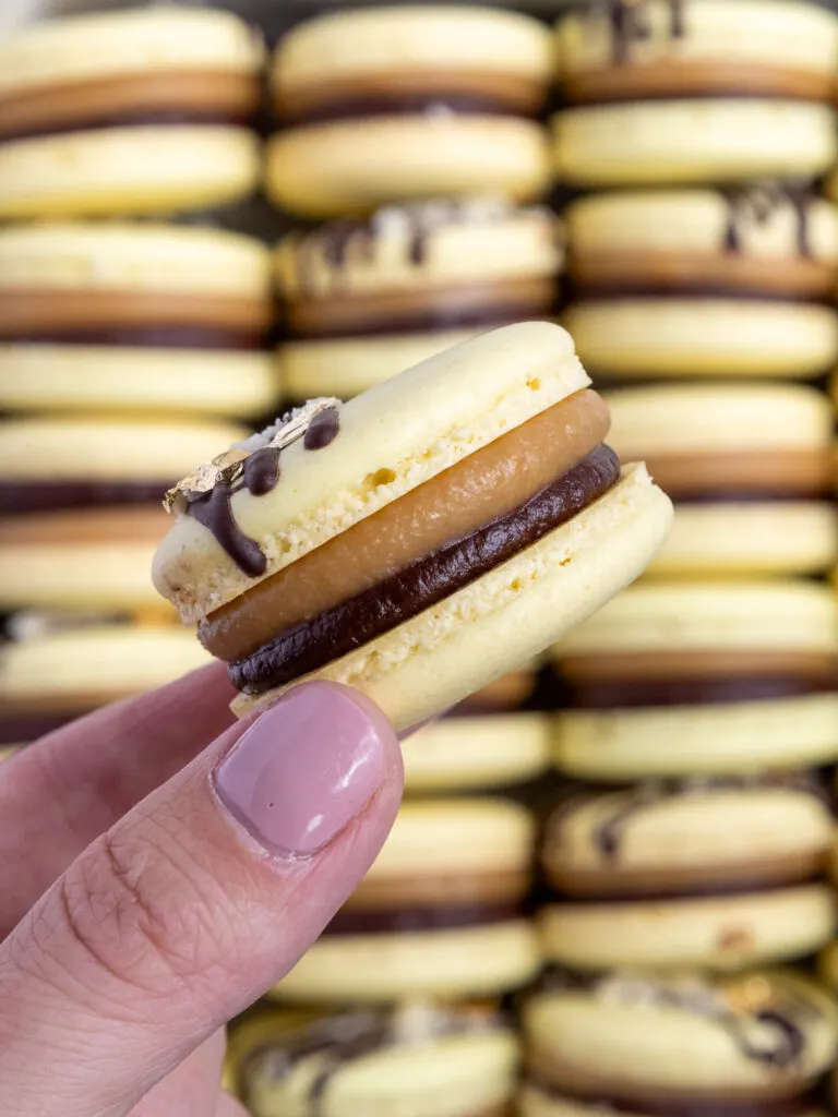 image of a millionaire macaron being held up to show its caramel and chocolate ganache filling