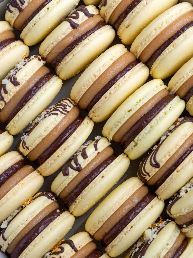 image of millionaire macarons stacked together in a tray to show their caramel and chocolate filling