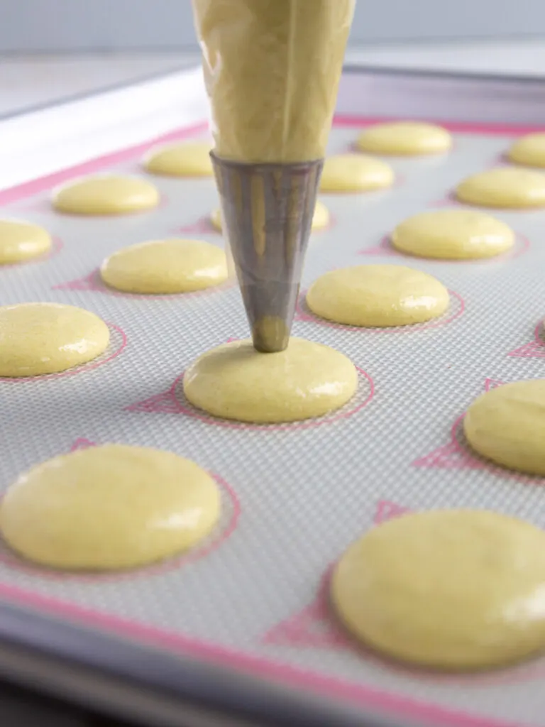 image of light yellow French macaron shells being piped onto a Silpat mat
