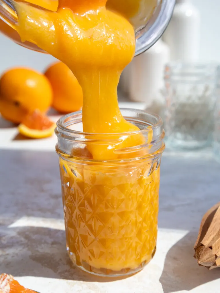 image of orange curd being poured into a glass mason jar