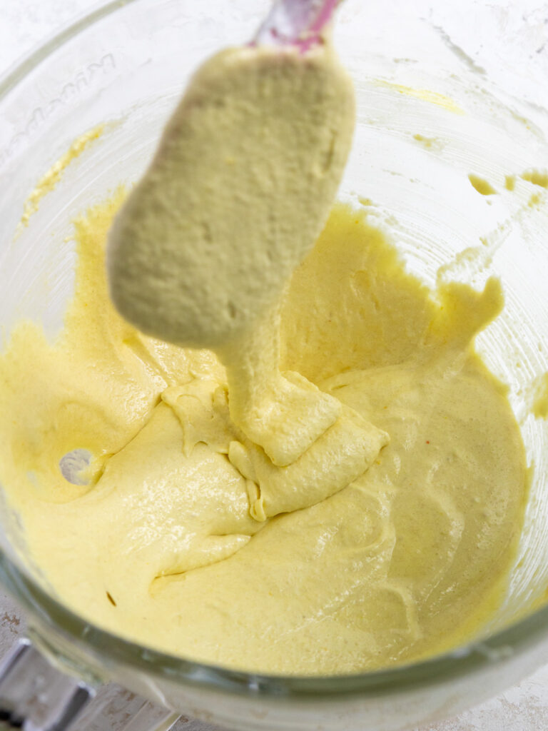 image of light yellow French macaron batter flowing off a spatula in thick ribbons