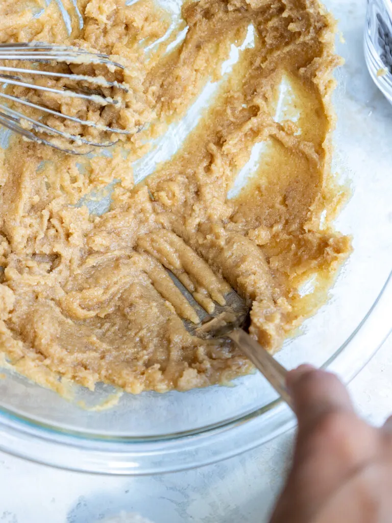 image of brown sugar chunks being broken up in cookie dough with a fork