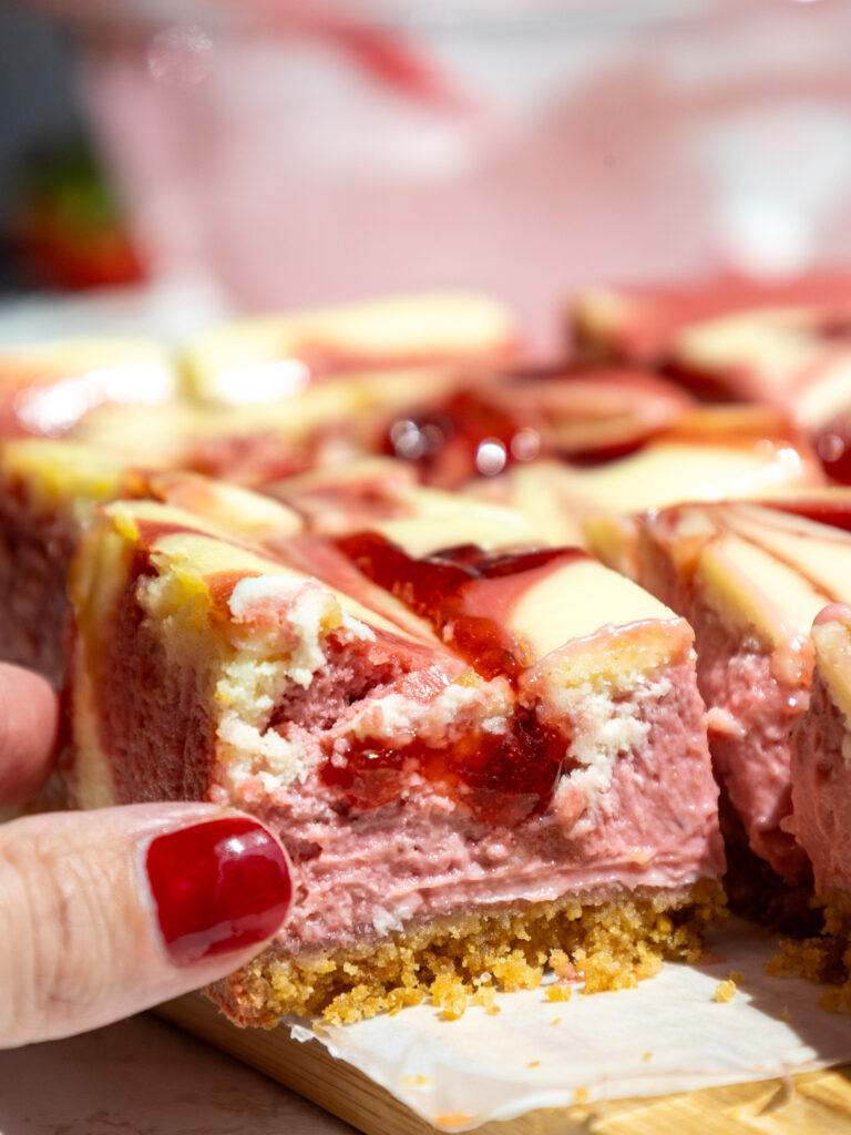 image of a strawberry cheesecake bar that's been cut into to show it's strawberry and regular cream cheese filling