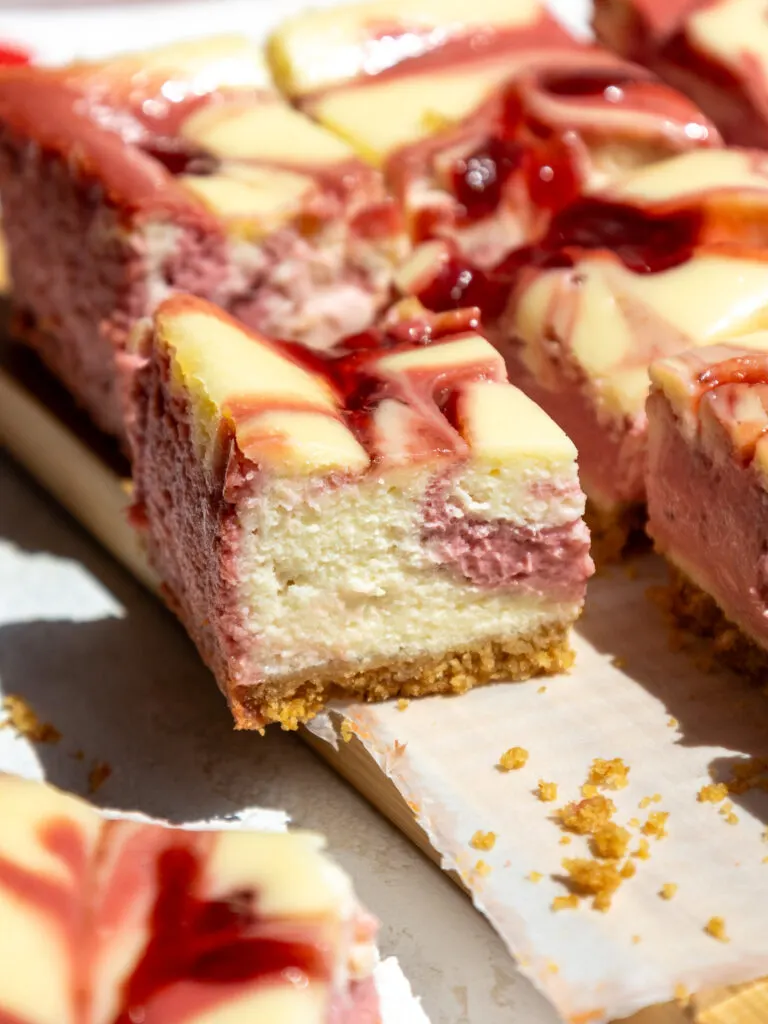 image of a strawberry cheesecake bar that's been cut into to show it's strawberry and regular cream cheese filling