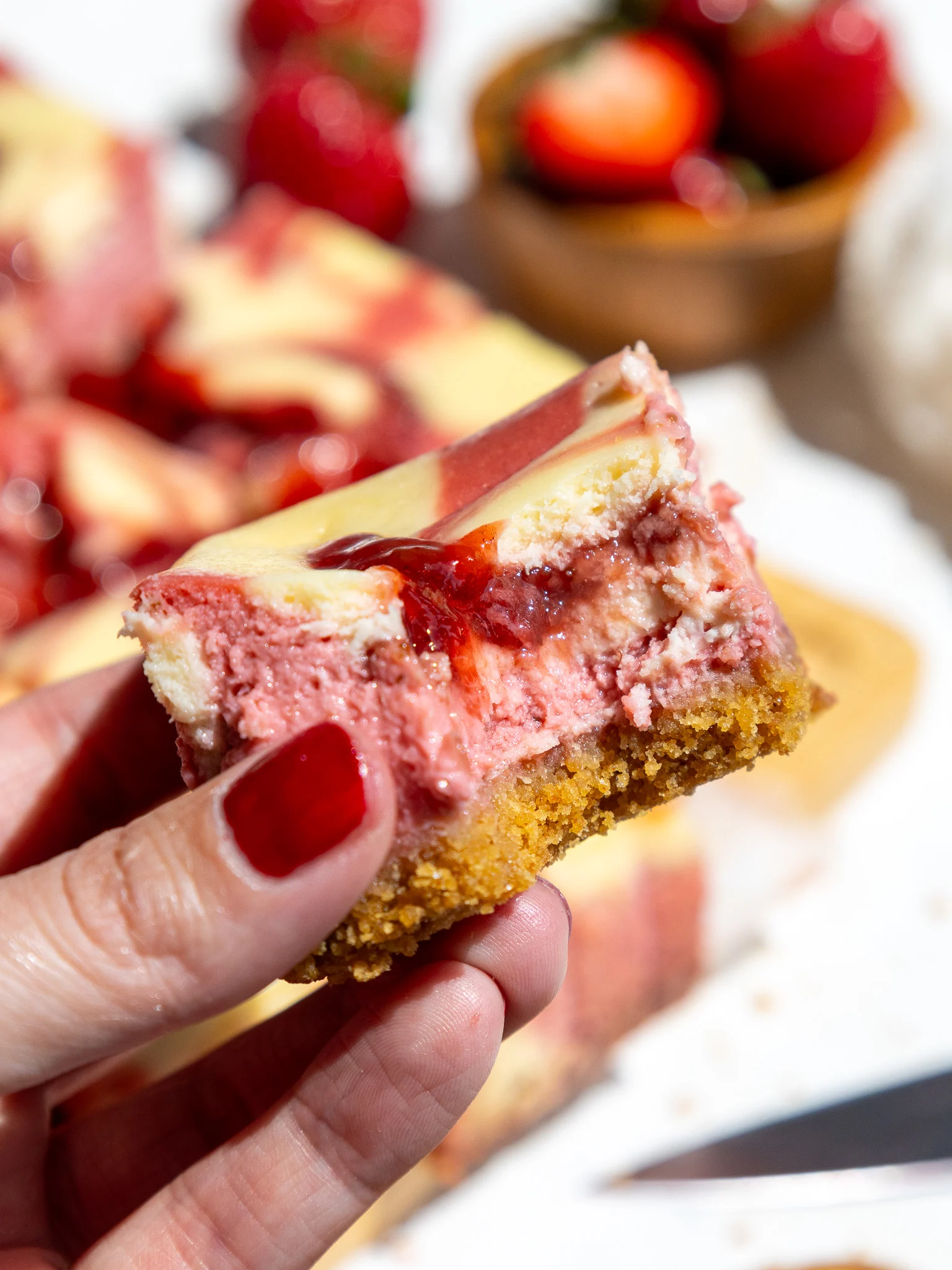 image of a strawberry cheesecake bar that's been bitten into to show it's strawberry and regular cream cheese filling