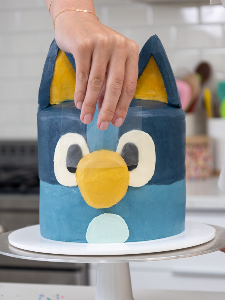 image of frosting on a Bluey cake being smoothed with an acetate sheet