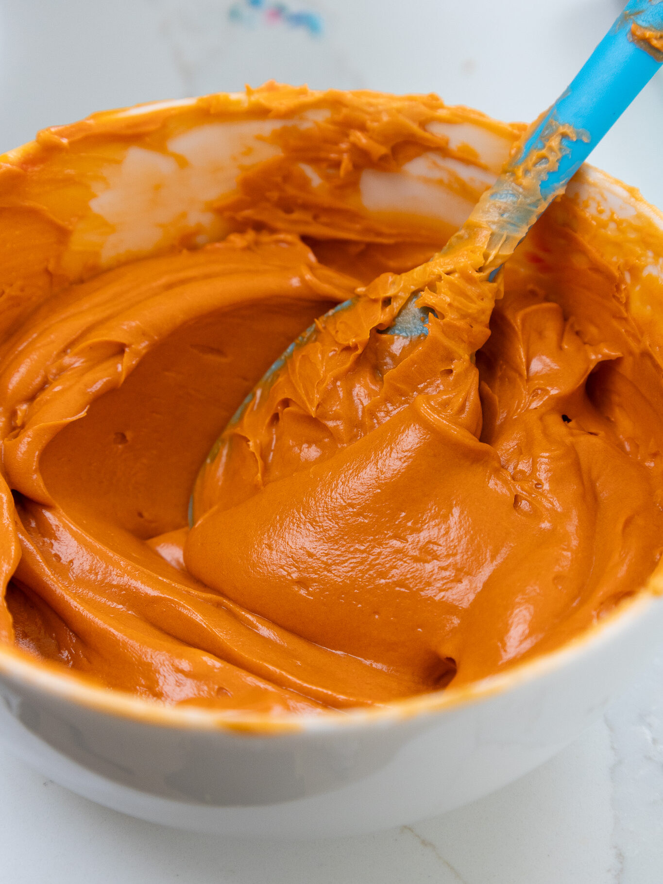 image of deep orange buttercream being colored with orange gel food coloring