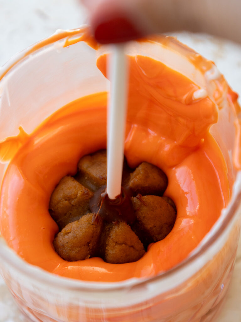 image of a pumpkin cake pop being dipped in orange colored white chocolate