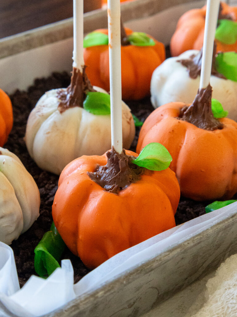 image of pumpkin cake pops sitting in a tray filled with oreo crumbs to look like a pumpkin patch