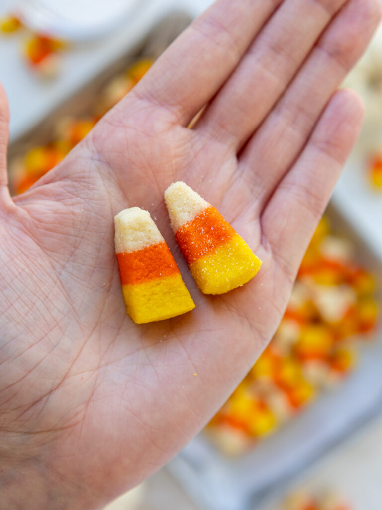 image of two candy corn cookies being held in a hand with one that was dunked in sugar