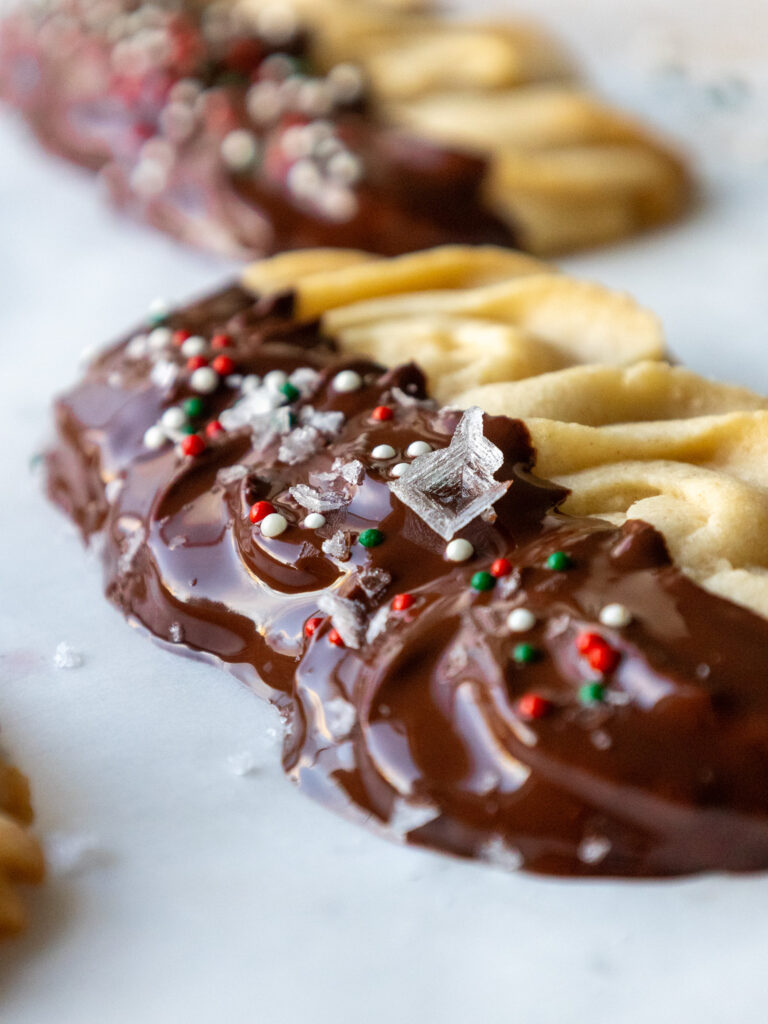 image of chocolate dipped butter cookies topped with a garnish of flakey sea salt and holiday sprinkles