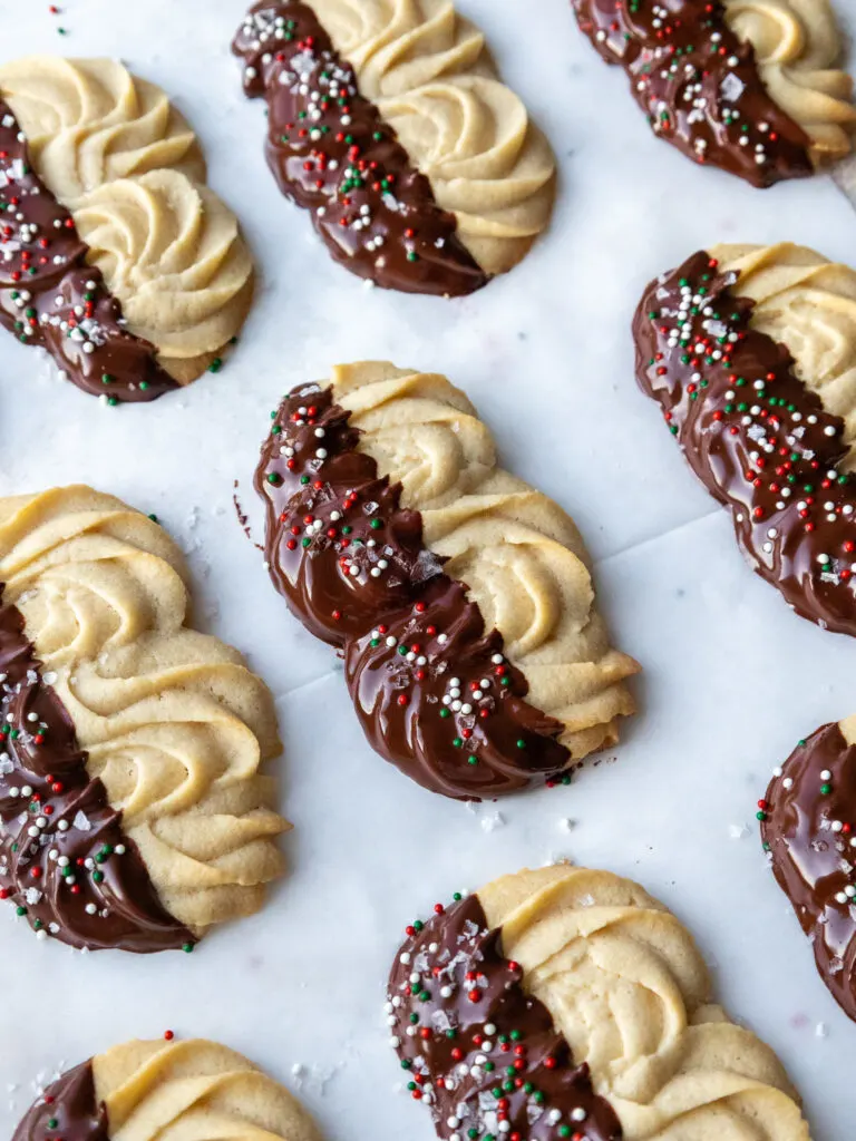 image of chocolate dipped butter cookies topped with a garnish of flakey sea salt and holiday sprinkles