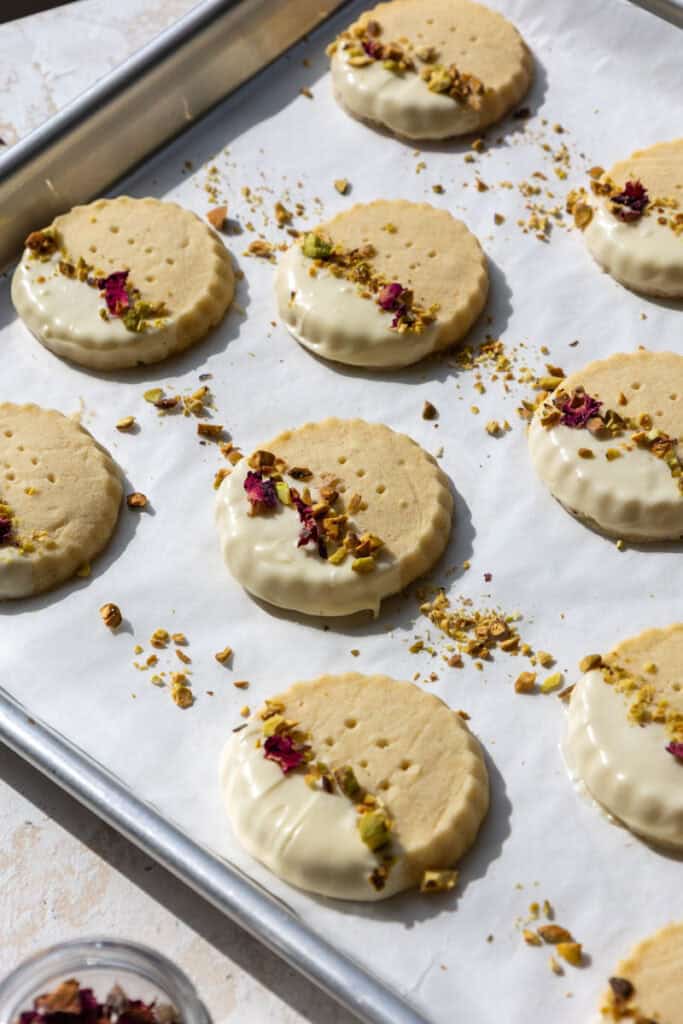 image of white chocolate dipped shortbread cookies that have been decorated with chopped pistachios and dried rose petals