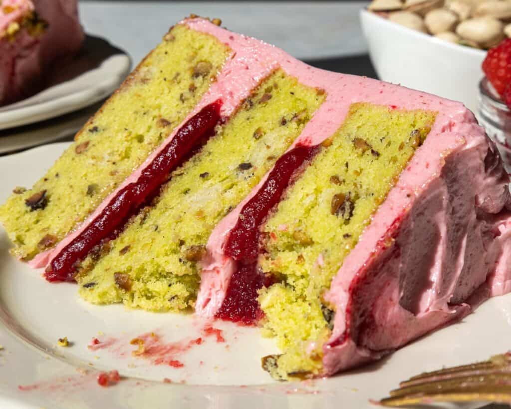 image of a raspberry pistachio cake slice that's been cut into to show it's filling and tender cake layers
